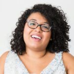 Happy businesswoman with curly hair using a laptop at her desk, smiling confidently.