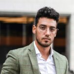 Elegant businessman in a green suit posing confidently on a city street with an urban background.